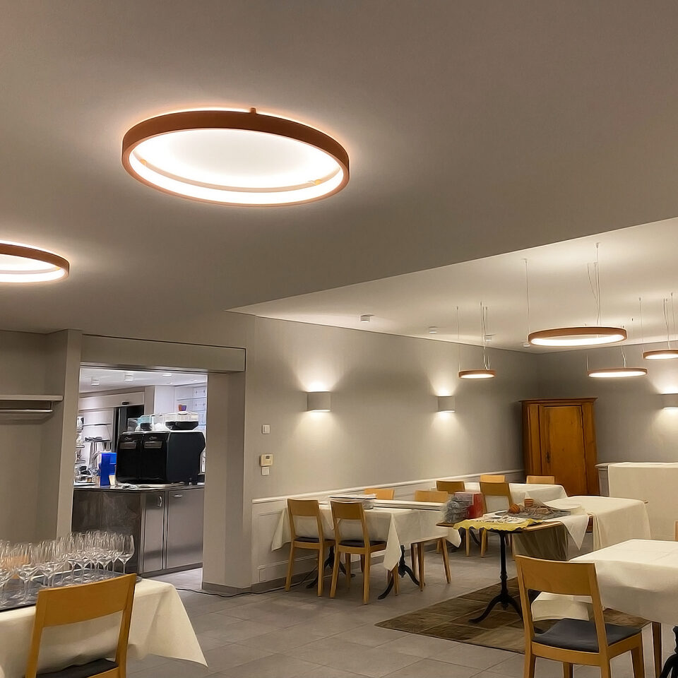 Corpuri de iluminat circulare cu ramă din lemn BPM Lighting instalate deasupra meselor la restaurantul Zur Kreuzstrasse