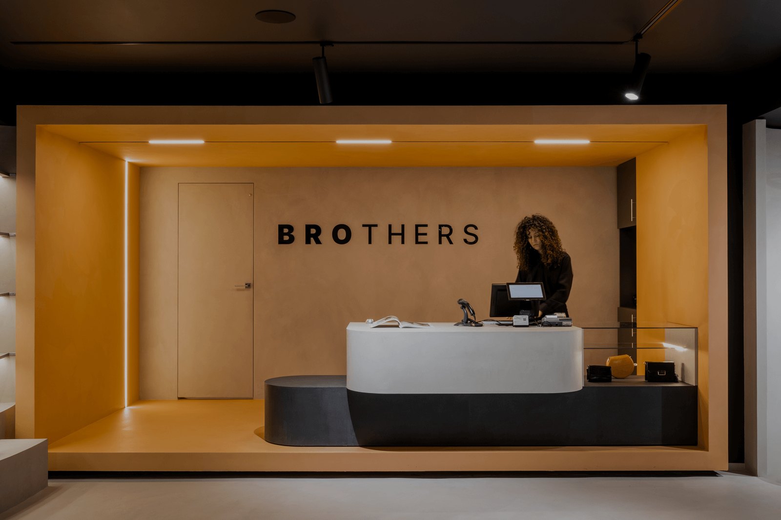 Зона ресепшн Brothers с логотипом на стене, нишей с тёплым цветовым акцентом и изогнутой стойкой
